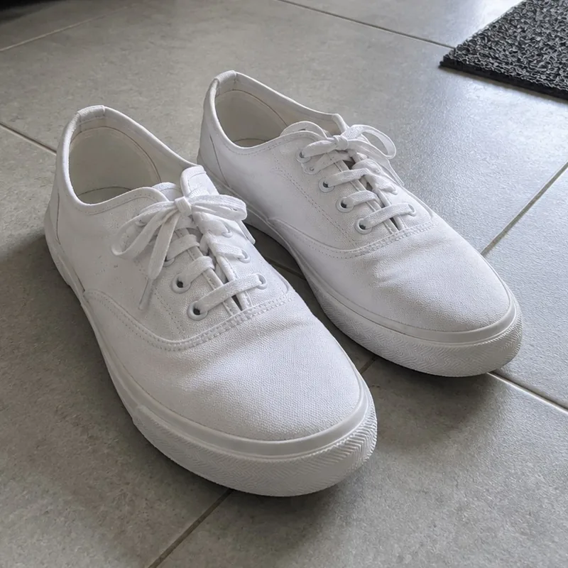 White sneakers on a tiled floor by the door, taken with a phone
